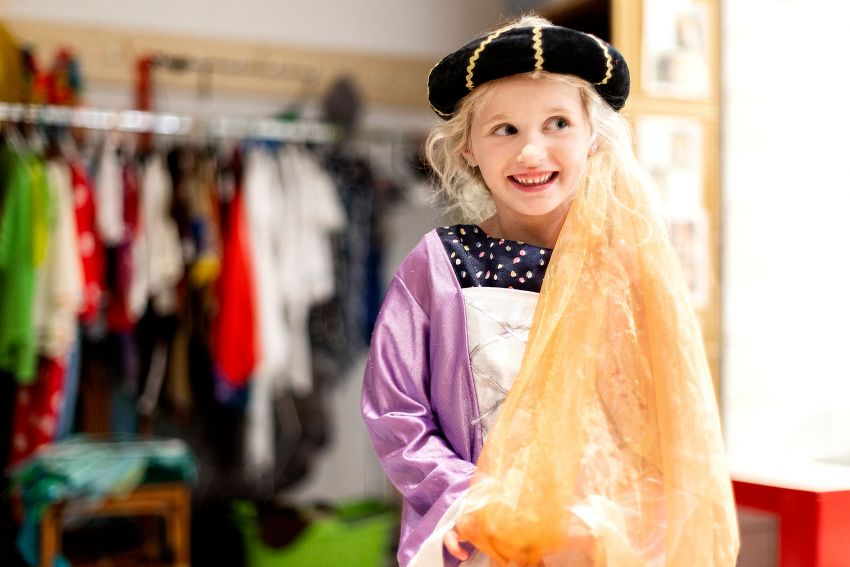 Ein junges Mädchen als Prinzessin verkleidet hält lächelnd ihre Schleppe vom Haarkranz in den Händen. Ein junges Mädchen als Prinzessin verkleidet hält lächelnd ihre Schleppe vom Haarkranz in den Händen.