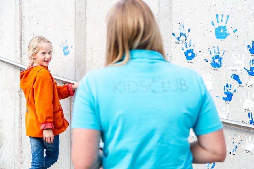 Ein junges Mädchen lächelt eine Frau im Vordergrund an, die ein hellblaues T-Shirt mit der Aufschrift  Ein junges Mädchen lächelt eine Frau im Vordergrund an, die ein hellblaues T-Shirt mit der Aufschrift