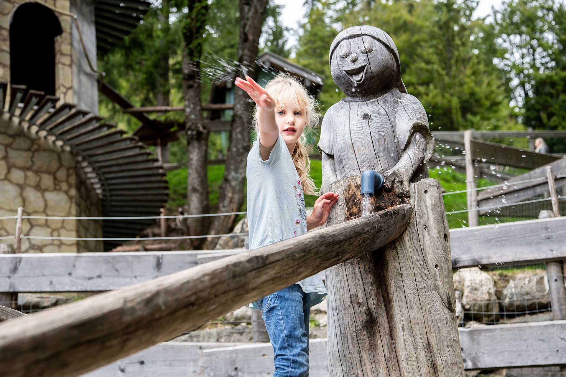 Ein junges Mädchen schnipst Wasser aus einem Brunnen in Form einer lustigen Figur umher. Ein junges Mädchen schnipst Wasser aus einem Brunnen in Form einer lustigen Figur umher.